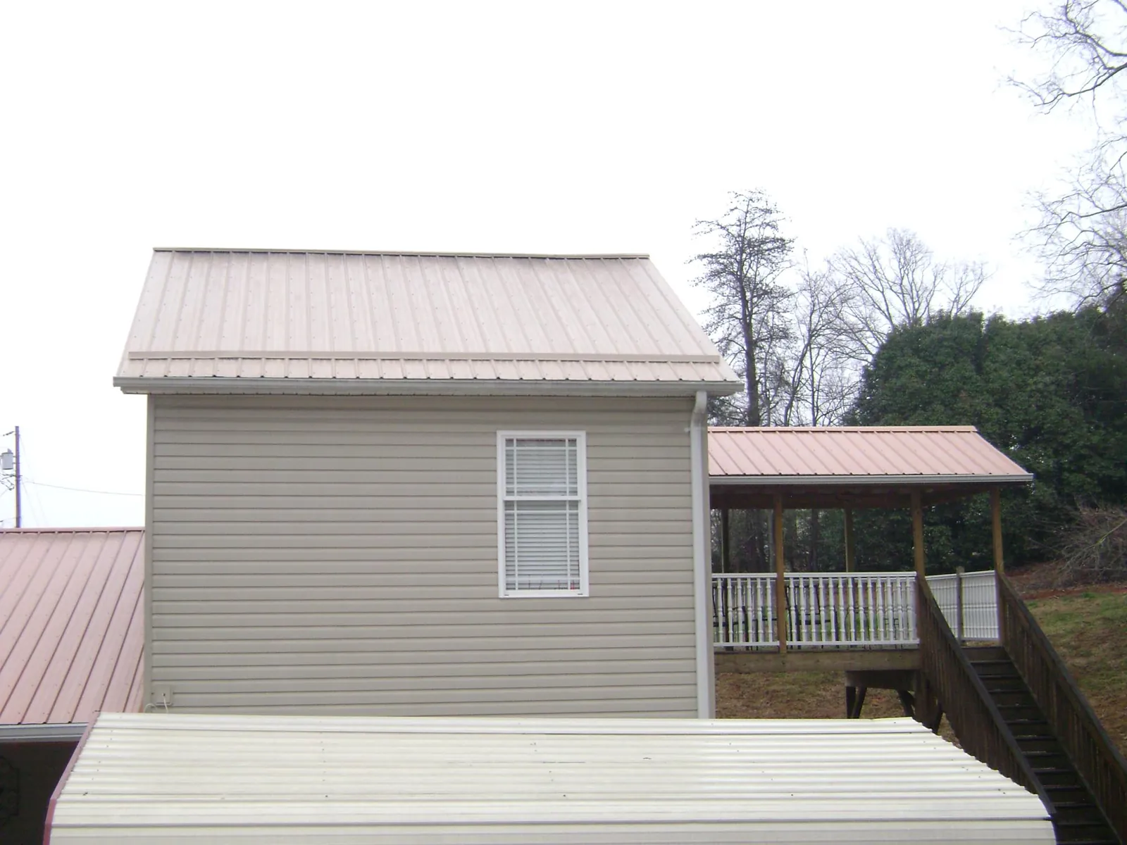 Tan metal roofs on a two story addition and attached porch, from a Roof Replacement job in Ashford